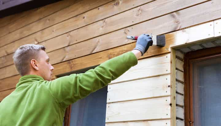 A professional painter using a long-handled brush to apply paint to the exterior of a house in Albuquerque.